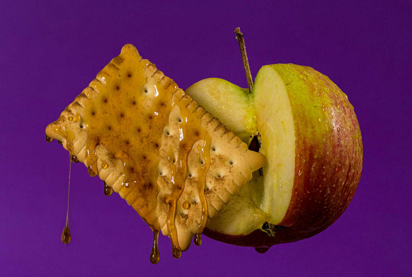 Apple, biscuit, a sprinkle of cinnamon and honey on purple background