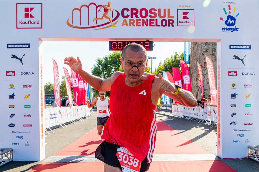 Alergator cu maieu rosu si numarul de concurs 3038 sarbatoreste cu bratele ridicate trecerea liniei de final la Crosul Arenelor 2025, sub poarta oficiala a evenimentului