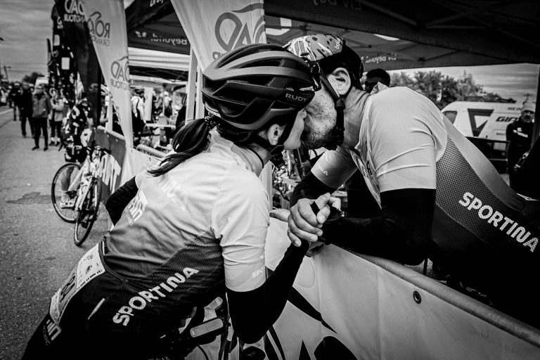 Seciu Mon Amour A black and white photo of a male and female cyclist sharing a kiss and holding hands at the end of Seciu Mon Amour road bike race.