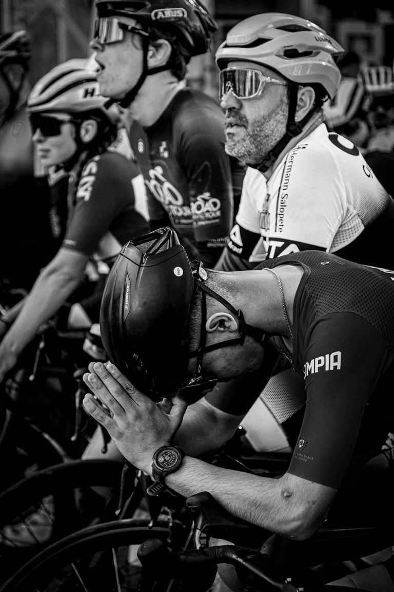 The Wall Ciclisti profesionisti aliniati la startul cursei The Wall 2025, purtsnd echipament complet de protectie si concentrare maxims inainte de competitie