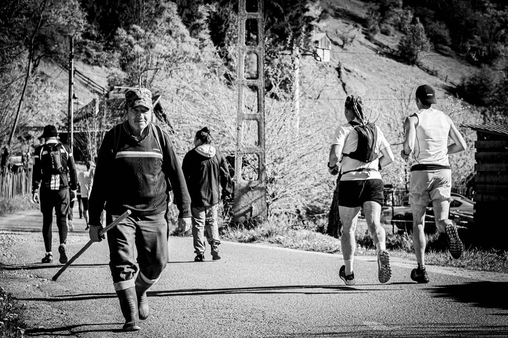 Concurenti la 1km de start la Eco Run 2026, fotografie alb-negru cu un satean care se ducea la munca si alergatori pe drum de munte