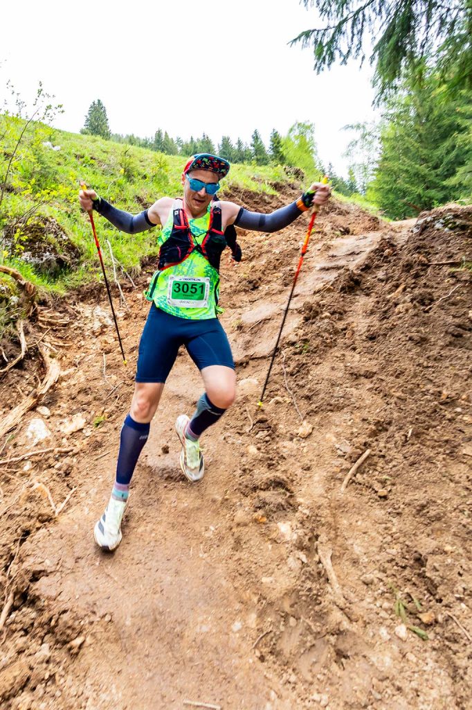 Concurent cu numarul 3051 coborand un traseu abrupt si noroios cu bete de trekking la EcoRun 2026, fotografiat de jos.