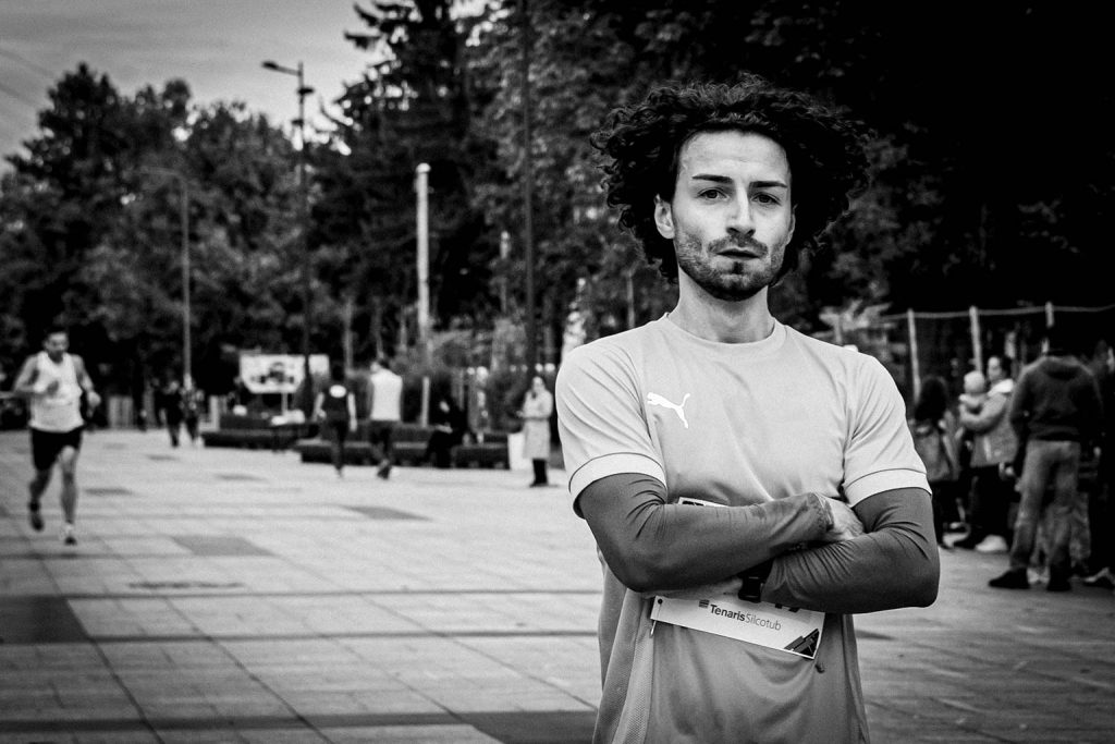 Concurent increzator cu bratele incrucisate la linia de finish a probei de 3km, purtand numar de concurs TenarisSilcotub, imagine alb-negru.