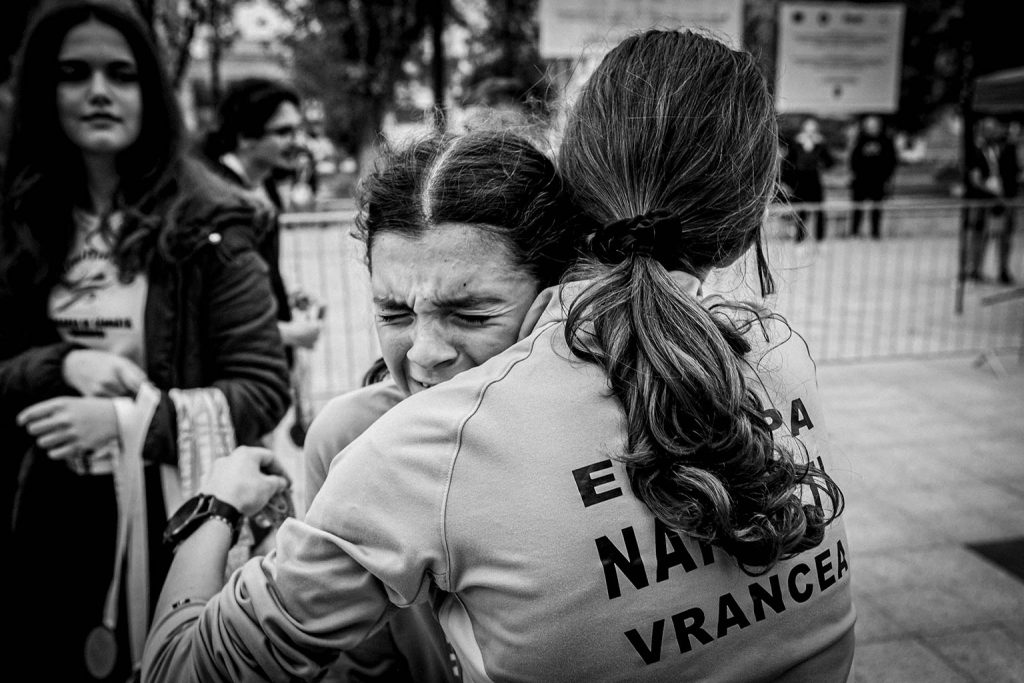 Concurenta de pe locul doi la proba de 3km imbratisata emotional dupa finish, purtand tricou cu inscriptia Echipa Nasol Vrancea, imagine alb-negru.