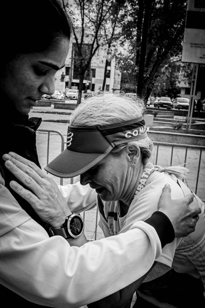Concurenta cu vizor si medalie, sprijinita de o alta persoana dupa terminarea dificila a probei de 10km la Calarasi, imagine alb-negru.