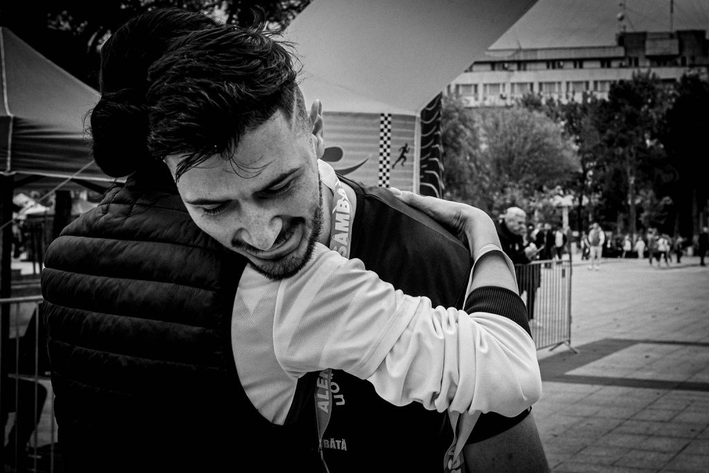 Concurent imbratisand o persoana dupa terminarea probei de semimaraton la Calarasi, cu medalia la gat, intr-o imagine alb-negru.