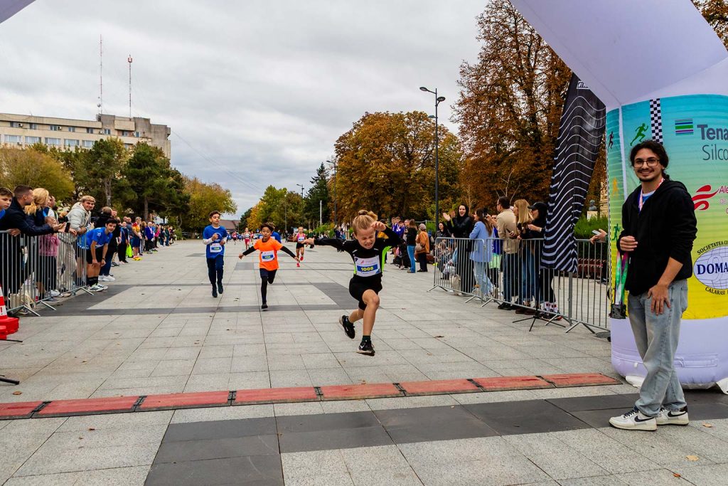 Castigatorul locul intai la Semimaratonul Alergarea de Sambata Calarasi, traversand linia de finish cu bratele ridicate, urmat de alti participanti