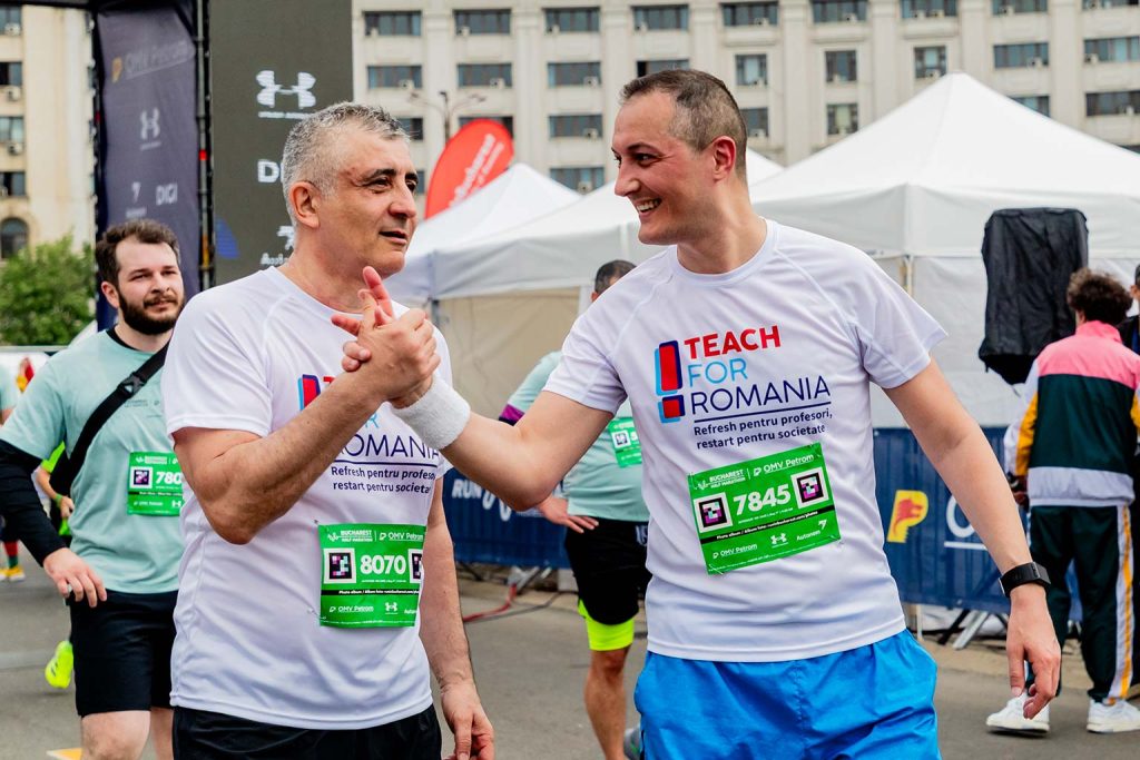 Doi participanti Teach For Romania cu numerele 8070 si 7845 schimband o strangere de mana la OMV Petrom Bucharest Half Marathon 2026.