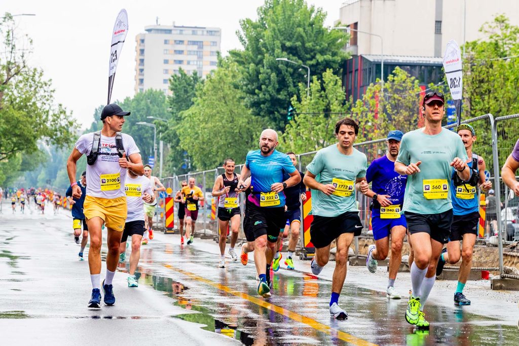 Alergatori la OMV Petrom Bucharest Half Marathon 2026 pe strada uda, inclusiv un participant cu tricou Teach For Romania.