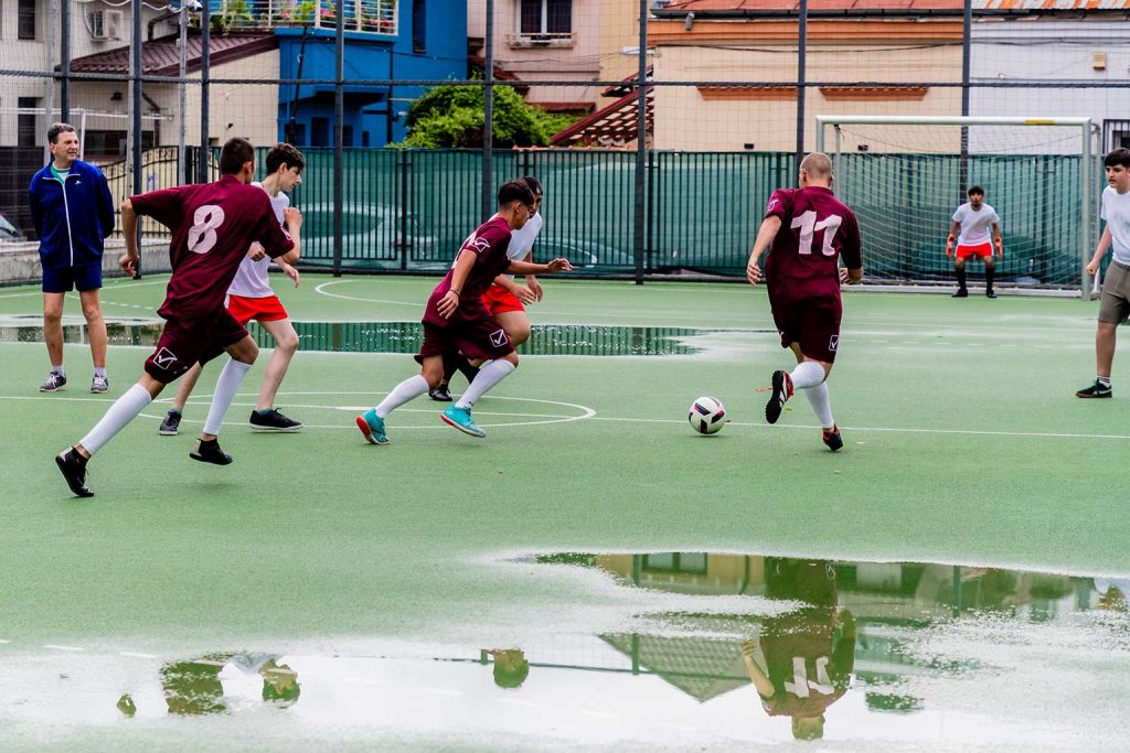 Jucatori de fotbal in actiune pe teren cu baltoace, echipa in marin cu numerele 8 si 11 alergand dupa minge la Campioni Speciali 2026