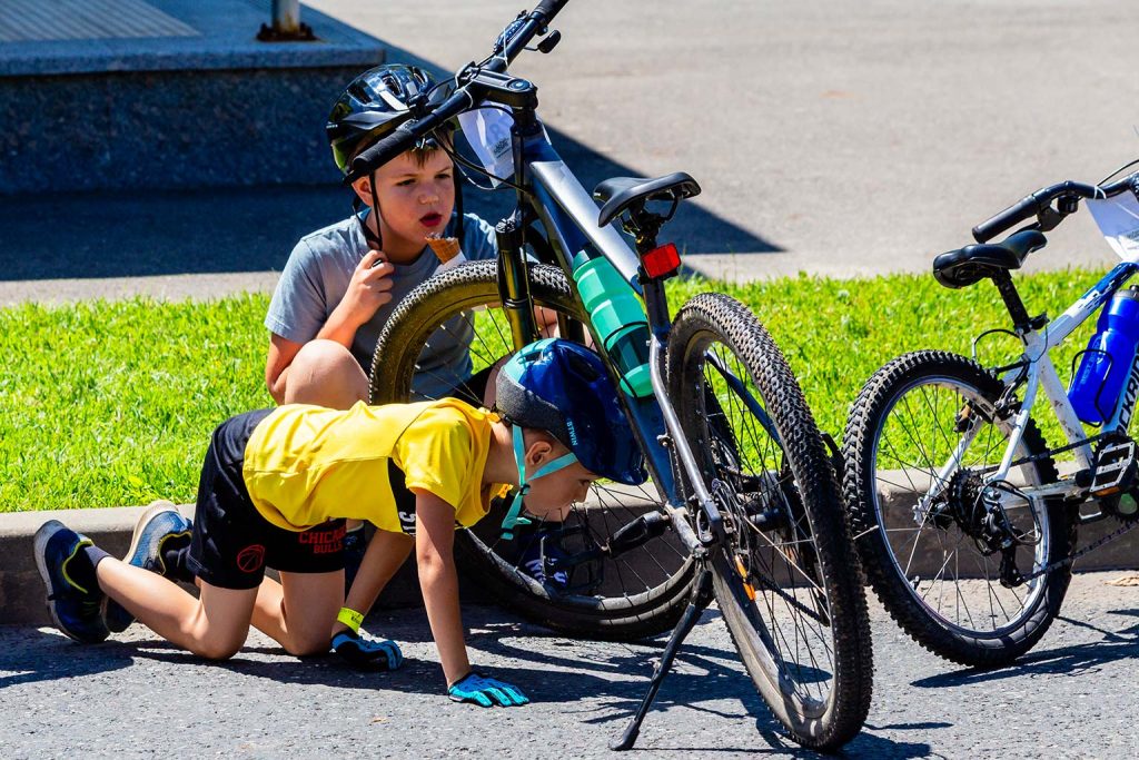 Inceputul Paradei Micilor Ciclisti, un copil in tricou galben examineaza roata bicicletei