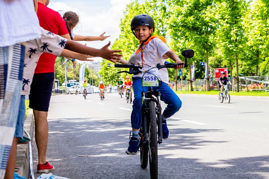 Copil cu numarul de concurs 2558 ofera high-five spectatorilor in timpul paradei micilor ciclisti