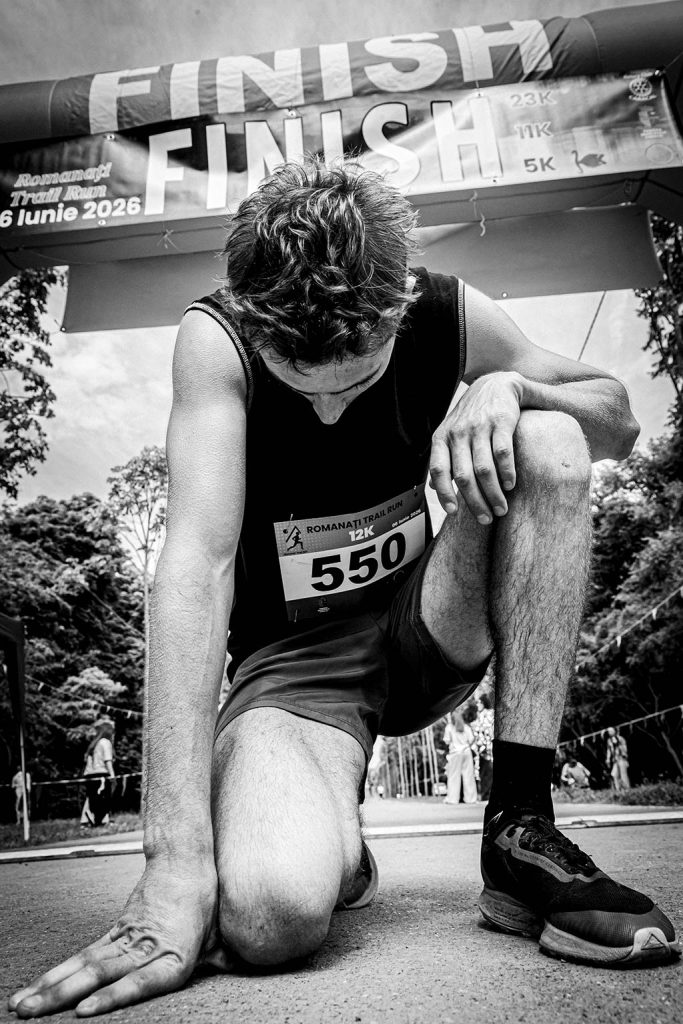 Fotograf sportiv Romanati Trail Run - concurent numar 550 epuizat si ingenuncheat sub arcada de finish proba 12km