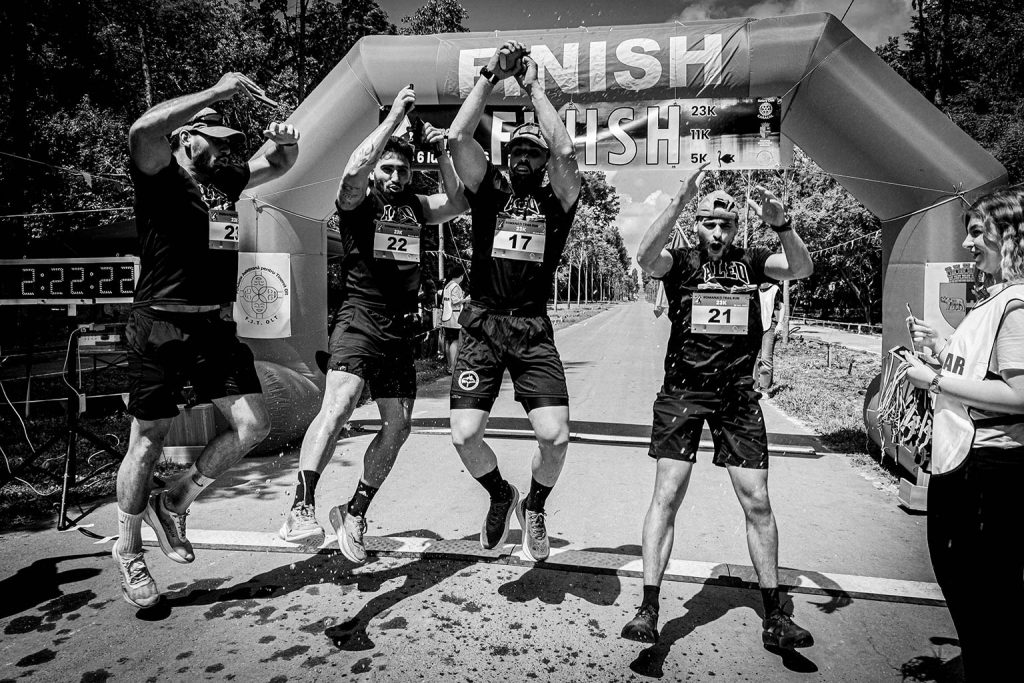 Fotograf sportiv Romanati Trail Run - echipa de alergatori sarind de bucurie sub arcada de finish dupa proba de 23km, numere 17, 21, 22