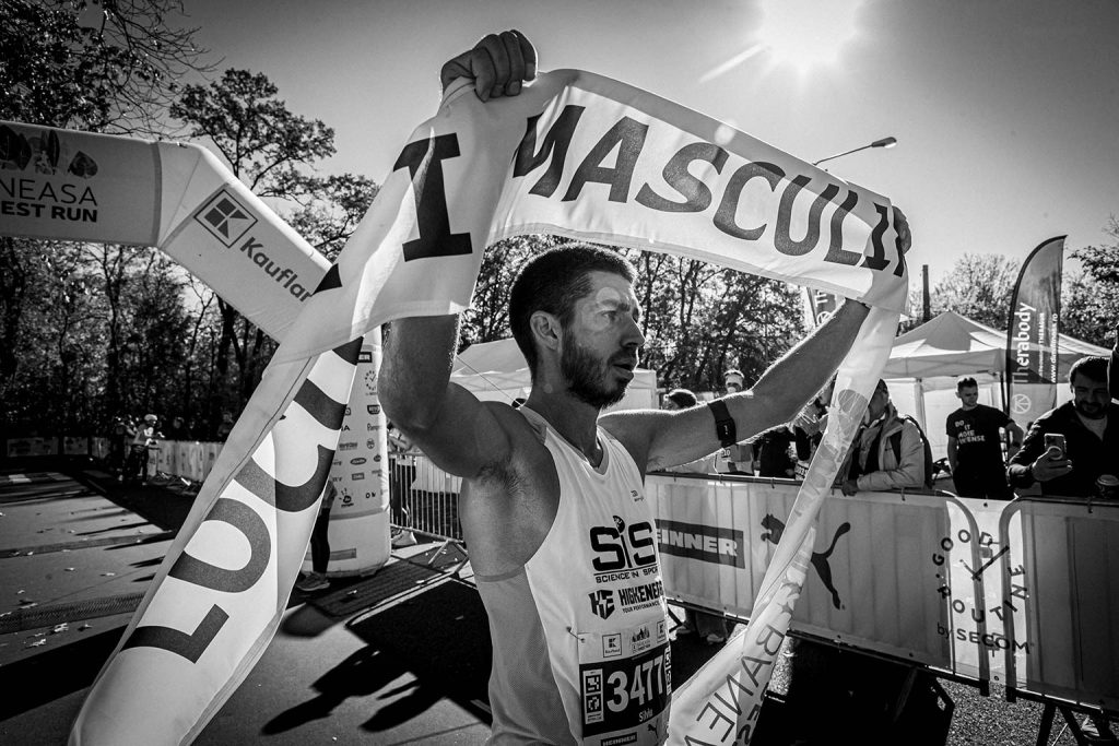 Fotografie sportiva la finish in cadrul Baneasa Forest Run 2025 - Castigatorul ridicand banda de finish deasupra capului, fotografie alb-negru