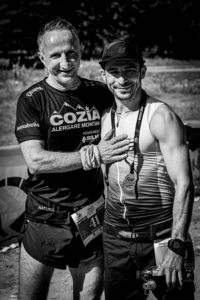 Doi concurenti zambitori, unul purtand medalia de finisher, asteptand festivitatea de premiere la Fuga Lotrilor.