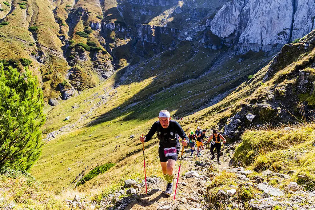 Alergator la Omu Marathon 2025 urcand pe un traseu montan stancos cu bete de trekking.