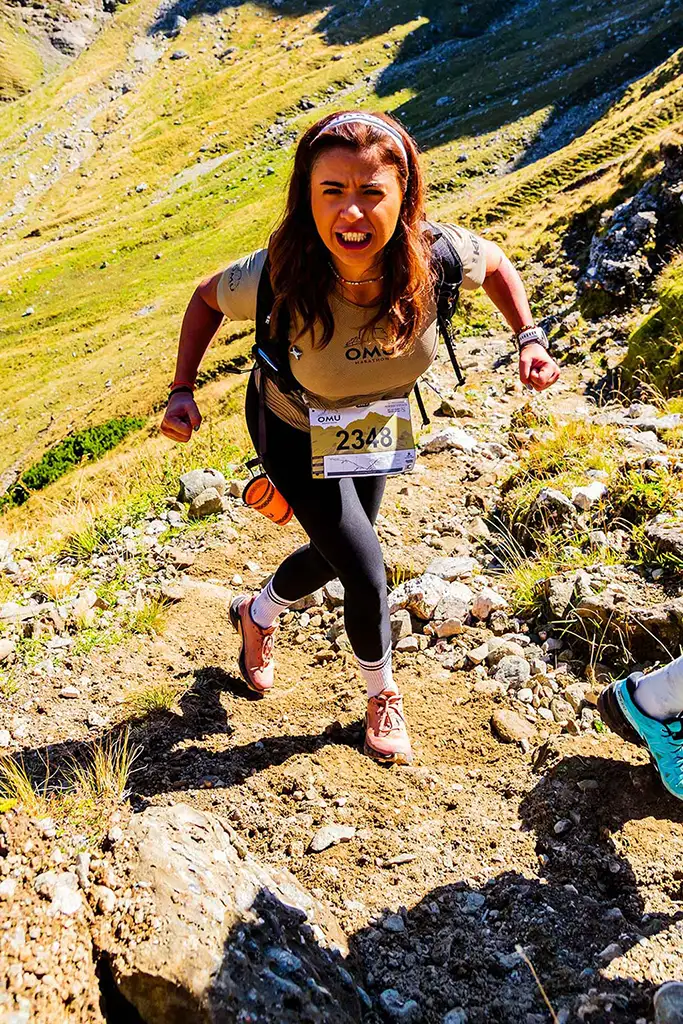 Alergatoare montana cu numarul 2348 urcand cu determinare pe poteca abrupta din Valea Ciubotea la Omu Marathon 2025, in lumina soarelui - fotografie sportiva color.